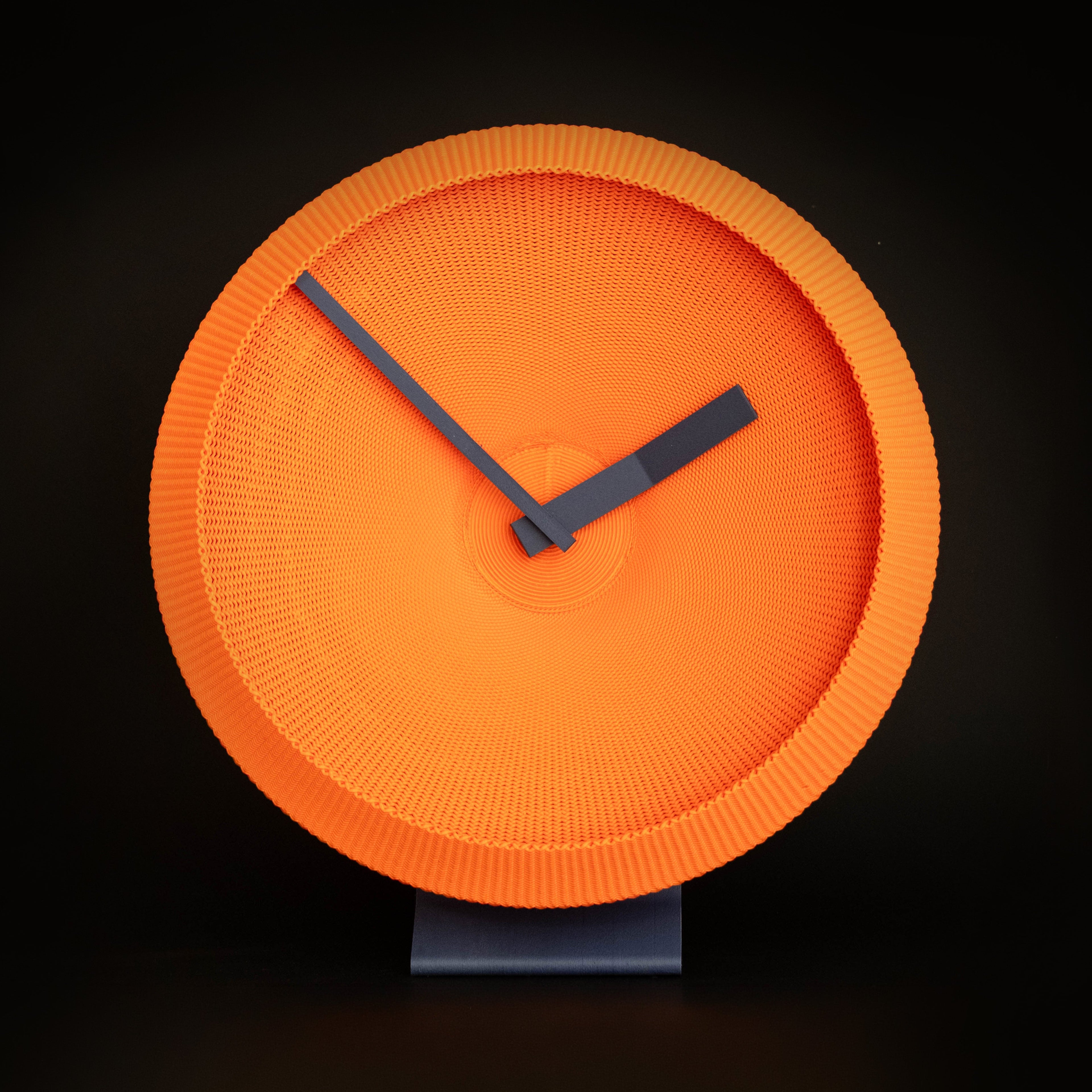 Orange 3D Printed clock with navy hands on a black background